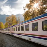 A picturesque train travels through a vibrant autumn landscape with mountains.