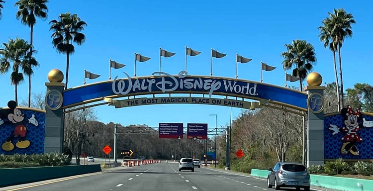 Colorful Walt Disney World entrance arch with Mickey and Minnie Mouse, palm trees, and blue sky.