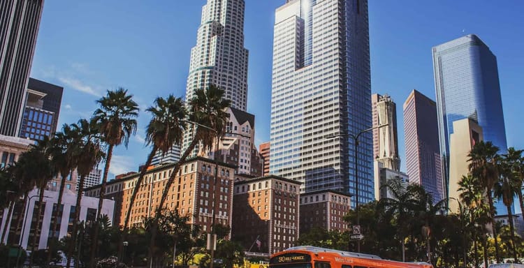 Vibrant Los Angeles cityscape with skyscrapers, palm trees, and Orange Metro bus on downtown streets.