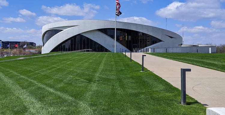 Modern performing arts center with a curved white façade and an American flag on a sunny day.