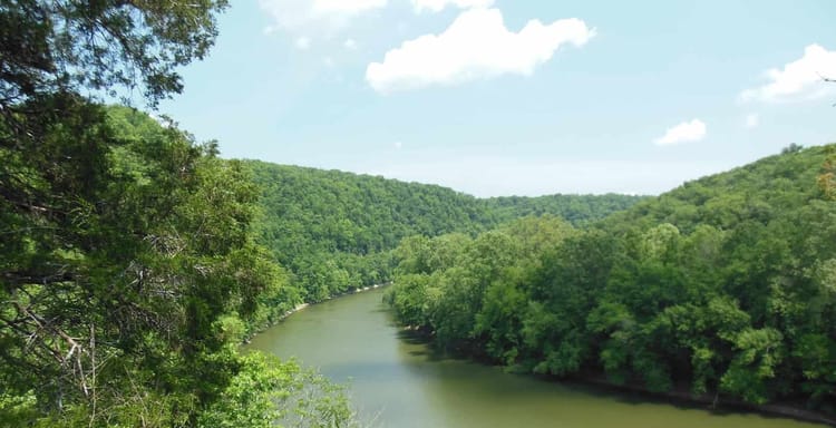 Serene river flowing through lush green forested hills, ideal for outdoor pursuits and nature exploration.