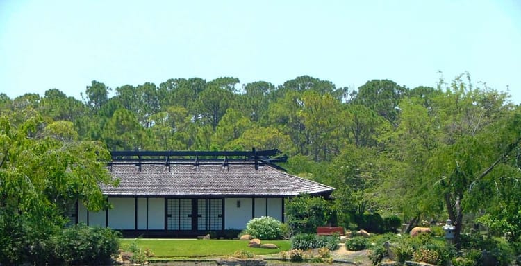 Serene Japanese-style garden with traditional pavilion by tranquil pond, lush greenery, perfect for relaxation and meditation.