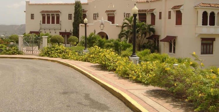 Elegant Spanish-style mansion with lush landscaping and classic street lamps, offering luxury real estate in a scenic location.