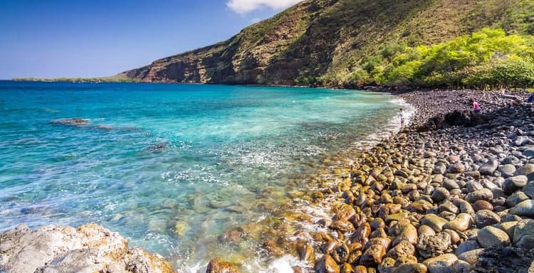 Pristine rocky beach with turquoise waters and lush green cliffs, perfect for relaxation and sightseeing.