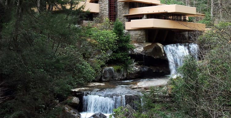 Modern house built on a rocky hillside with waterfalls and lush greenery surrounding it.