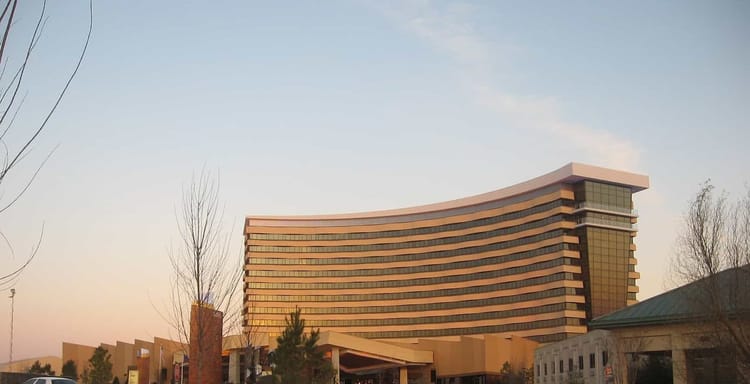 Modern hotel building with curved architecture and surrounding parking lot at sunset.