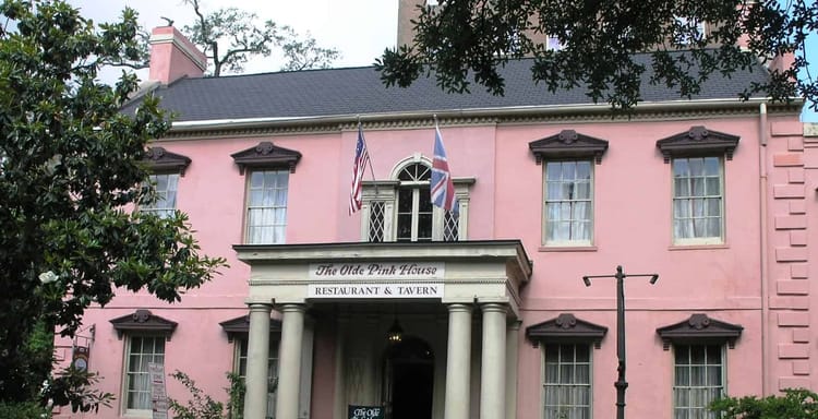 Colorful pink historic restaurant building with flag displays and colonial architecture, offering a charming dining experience.