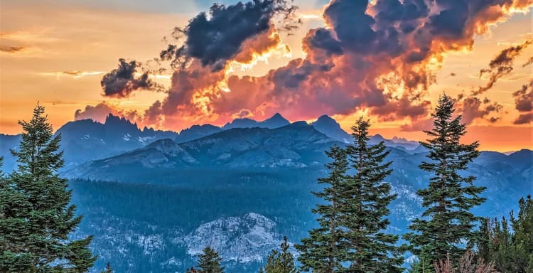 Vivid mountain sunset with dramatic clouds, pine trees, and colorful sky in wilderness.