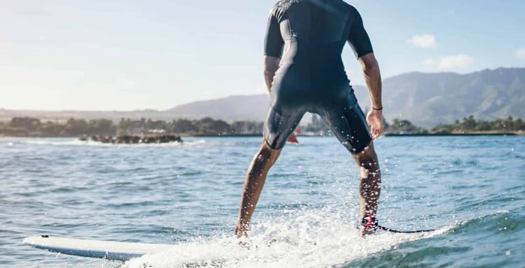 Surfer riding a small blue wave under clear sky near Fort Lauderdale beach.