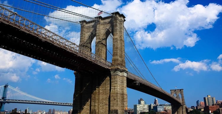 Iconic Brooklyn Bridge connecting Manhattan and Brooklyn in New York City under blue sky with clouds.