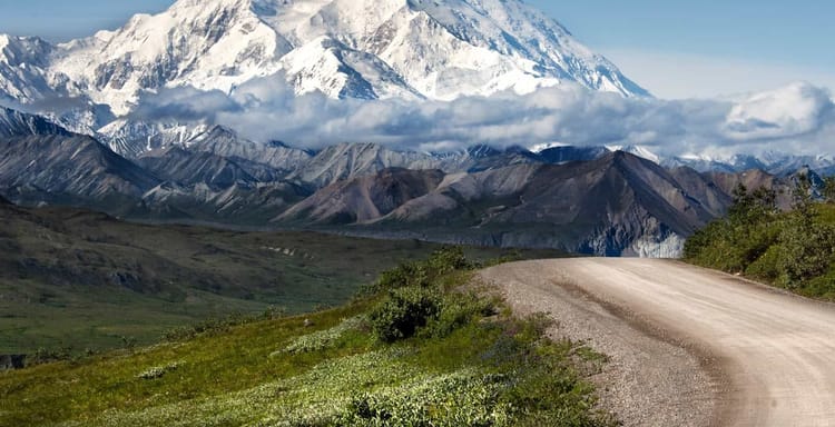 Snow-capped mountain landscape, rugged terrain, winding dirt road, adventure travel, scenic wilderness.