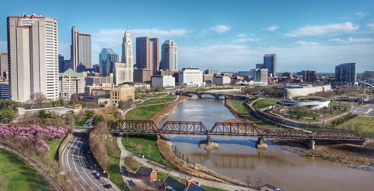 Aerial view of Columbus Ohio skyline with river, parks, and city buildings.
