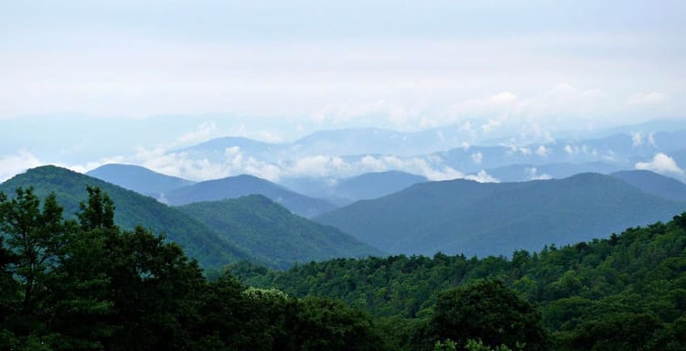 Vast green mountain landscape with rolling hills and lush forest under a cloudy sky.