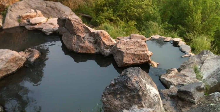 Serene backyard hot tub surrounded by rocks with lush green trees in the background.