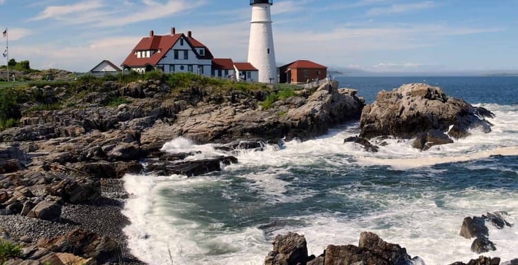 Lighthouse near rocky coast with ocean waves in the background, scenic seaside travel destination.