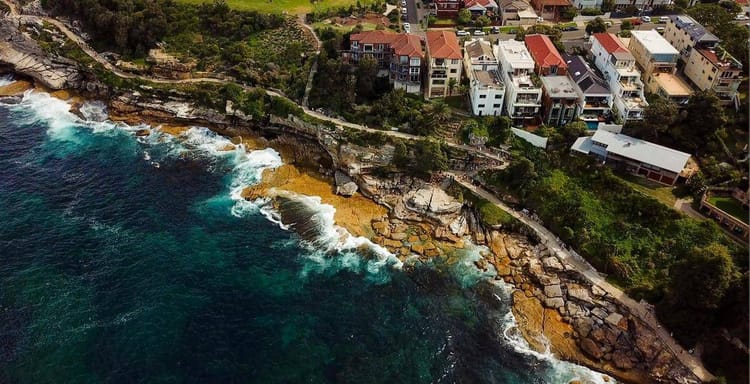 Cliffside residential neighborhood overlooking ocean with rocky shoreline and modern homes.