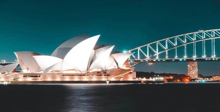Sydney Opera House illuminated at night with Harbour Bridge, iconic tourist destination in Australia.
