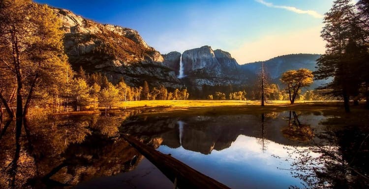 Majestic mountain landscape with waterfall, trees, and reflection in serene water setting.