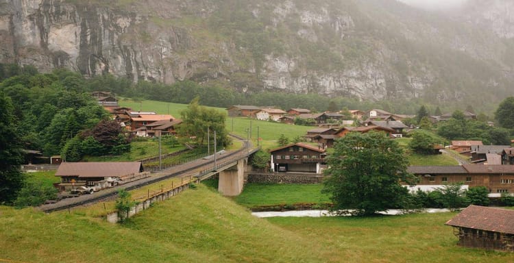 Charming Swiss village nestled in lush green hills with railway and mountain backdrop.