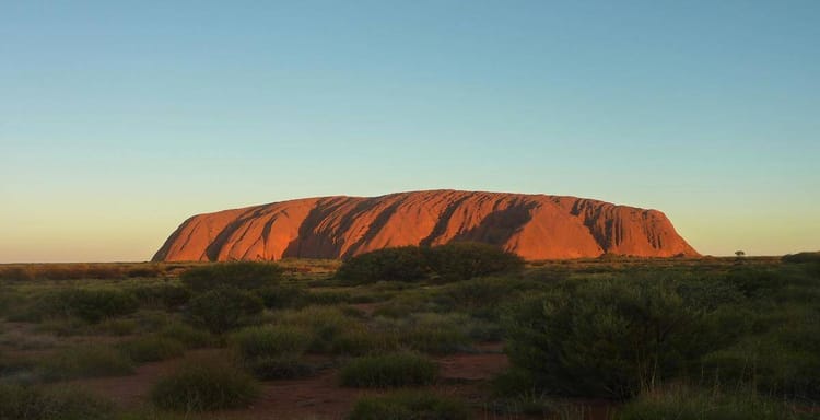 Ancient Uluru rock formation in Australia's desert landscape at sunset.