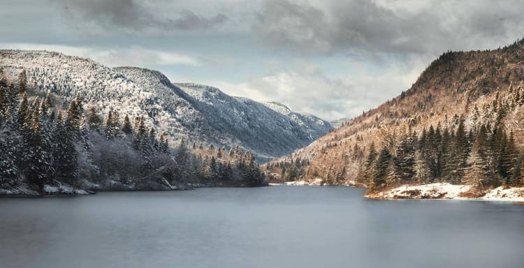 Snow-covered mountain landscape with a calm river and dense pine forests, perfect for outdoor adventures.
