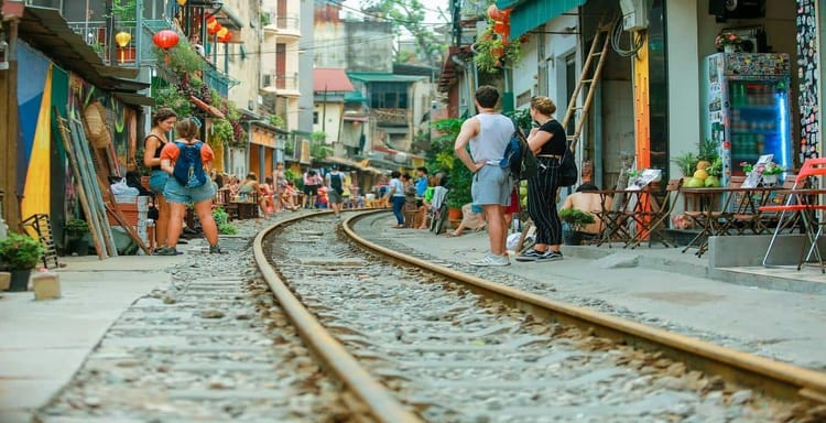 Colorful urban street scene with railway tracks, tourists, and local shops in a vibrant neighborhood.