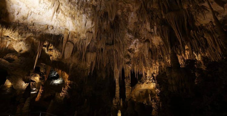 Ancient cave formations with stalactites and stalagmites, illuminated inside a natural underground cavern.