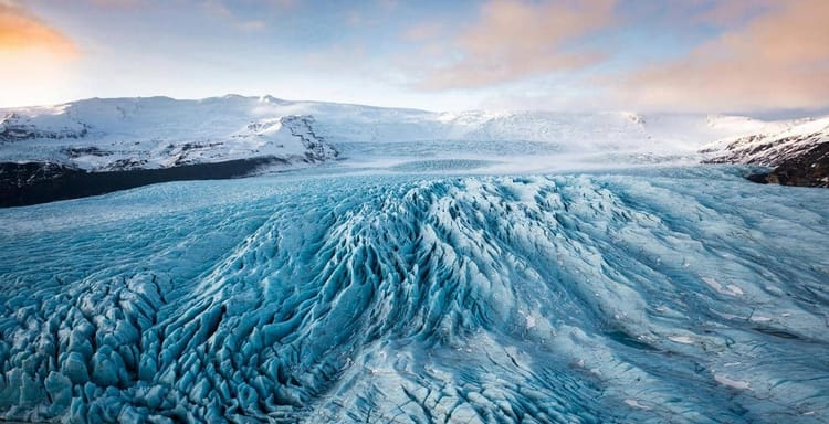 Mighty glacier in Iceland with snow-covered mountains and vibrant sky in the background.