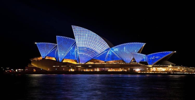 Brightly lit Sydney Opera House illuminated with vibrant blue lights at night, iconic Australian landmark.