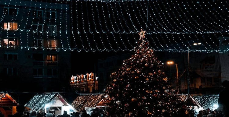 Festive Christmas market with decorated tree, string lights, and holiday shoppers at night.