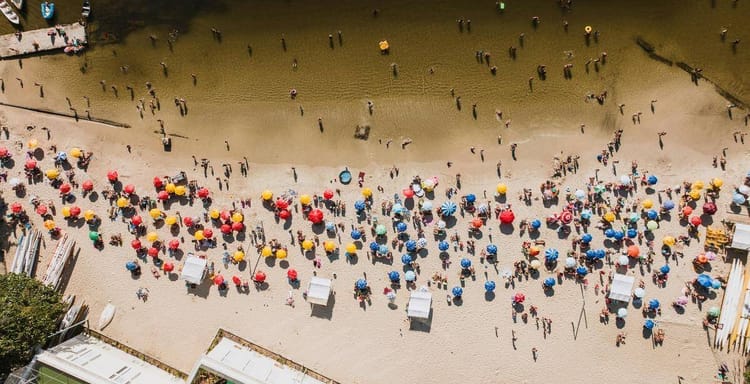 Colorful beach umbrellas and visitors at a sandy shoreline, sunny summer day, outdoor leisure, popular beach destination, QuestForDirections.