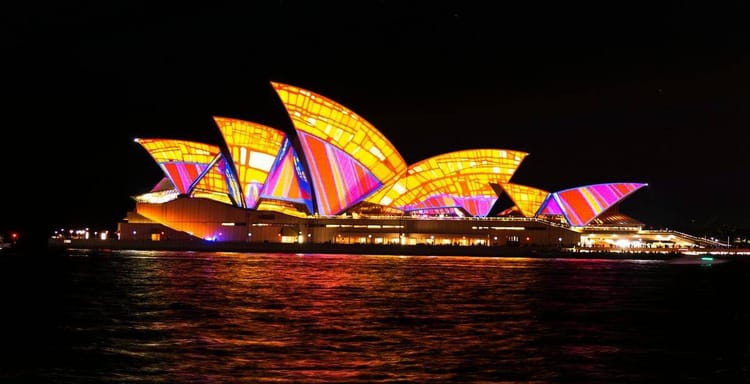 Colorfully lit Sydney Opera House illuminated at night with vibrant light display.