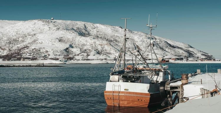 Snow-covered harbor with a boat, scenic mountain view, Norway, winter maritime landscape.