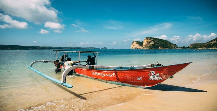 Colorful surfboat on sandy beach with tropical island scenery in background.