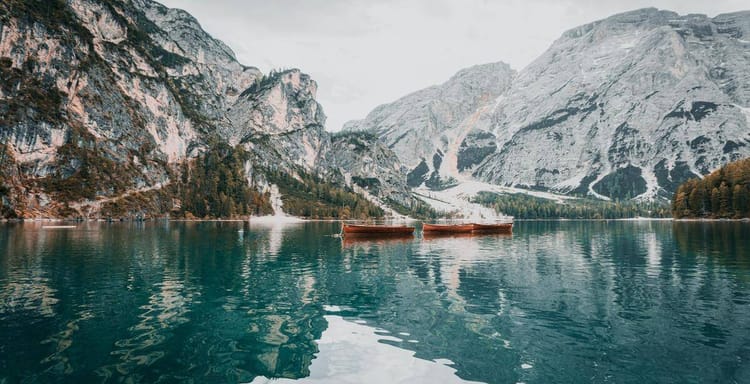 Serene mountain lake with boats, scenic alpine landscapes, and crystal-clear waters in a tranquil outdoor setting.