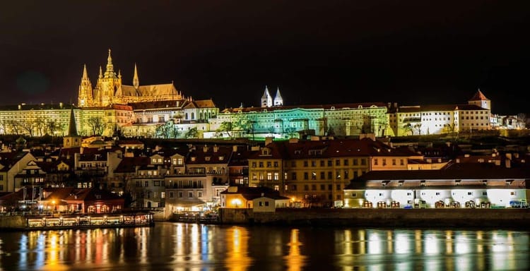 Colorful illuminated Prague Castle at night with reflections in Vltava River, Czech Republic.