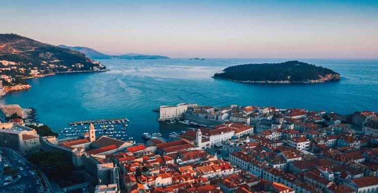 Panoramic view of Dubrovnik Old Town with red rooftops, fortress walls, and Adriatic Sea coastline.