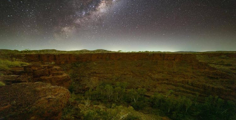 Stargazing over a desert canyon at night with the Milky Way in the sky.