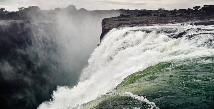 Vast waterfall cascading into river with lush forest backdrop, scenic natural landscape.