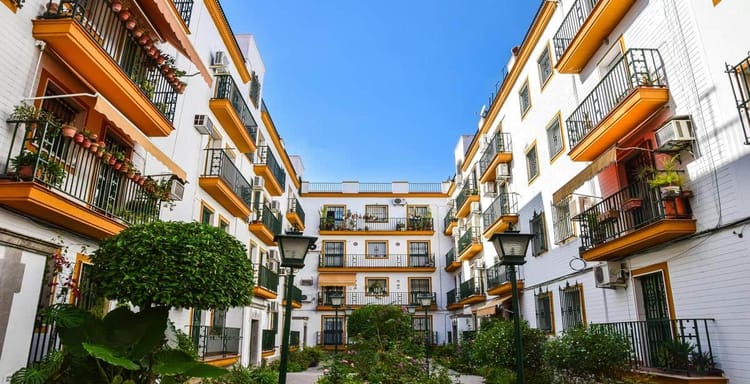 Colorful apartment buildings with balconies and lush greenery in a sunny urban courtyard.