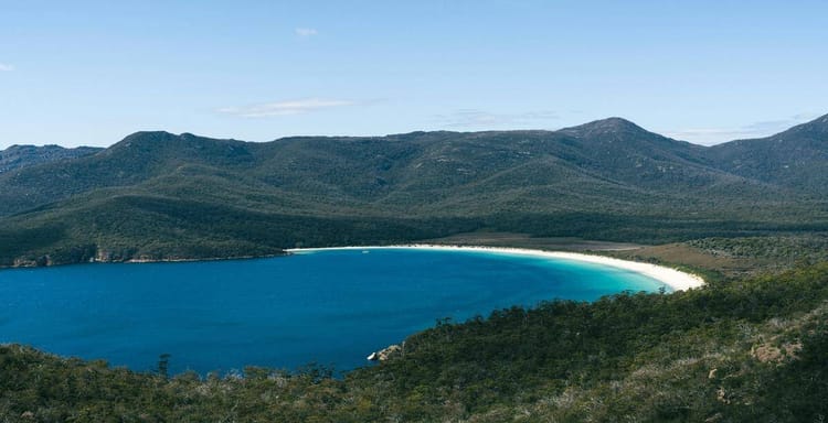 Pristine beach and turquoise waters around scenic wilderness bay with lush green mountains.