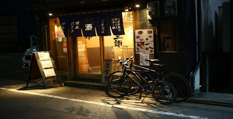 Cozy Japanese restaurant entrance with bicycles outside, illuminated at night, featuring traditional noren curtains.