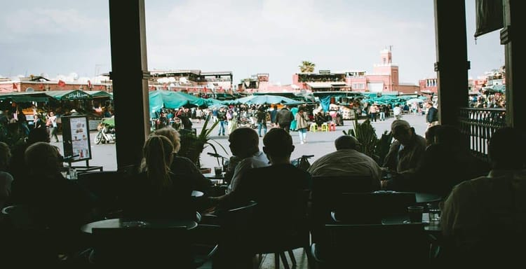 Busy market scene with outdoor vendors and shoppers, view from a café window in Morocco.
