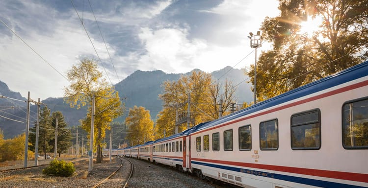 A picturesque train travels through a vibrant autumn landscape with mountains.