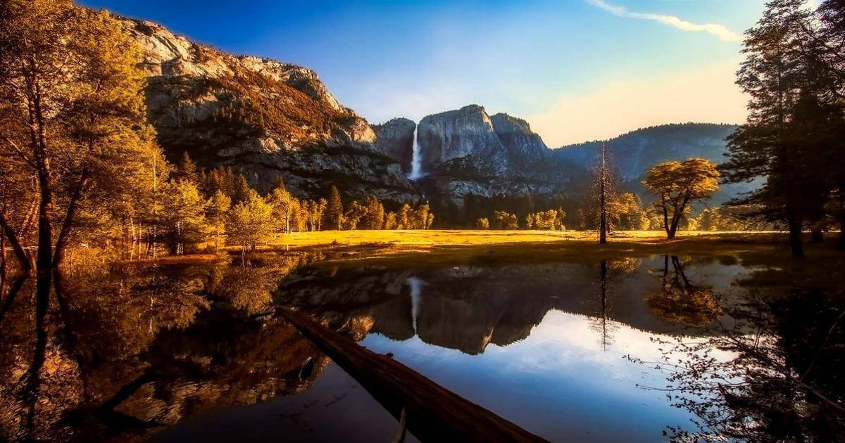 Majestic mountain landscape with waterfall, trees, and reflection in serene water setting.