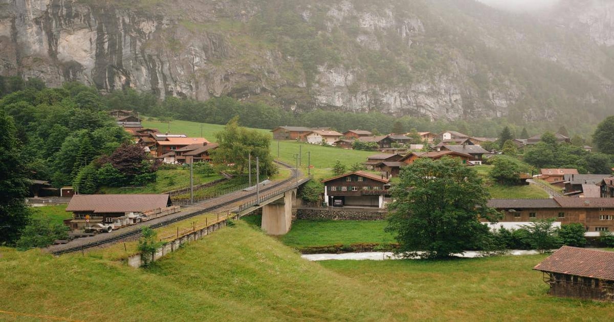 Charming Swiss village nestled in lush green hills with railway and mountain backdrop.