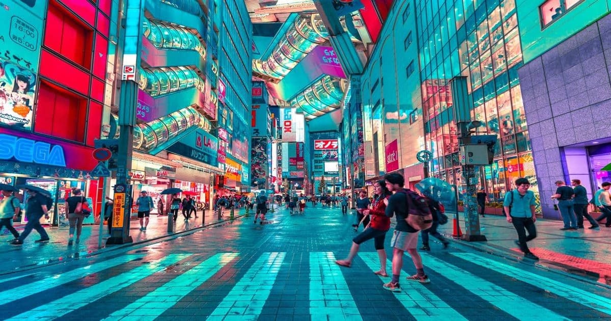 Vibrant Tokyo street scene with neon signs, busy crosswalk, and pedestrians in summer rain.