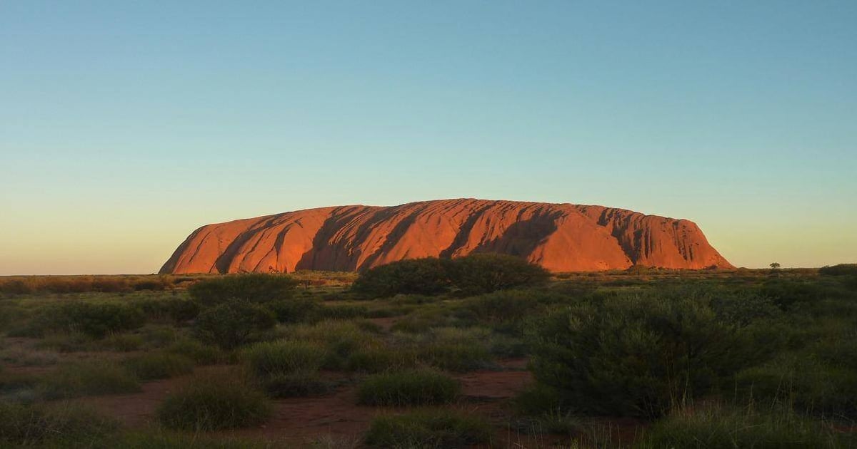 Ancient Uluru rock formation in Australia's desert landscape at sunset.