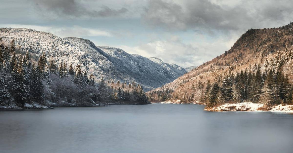 Snow-covered mountain landscape with a calm river and dense pine forests, perfect for outdoor adventures.