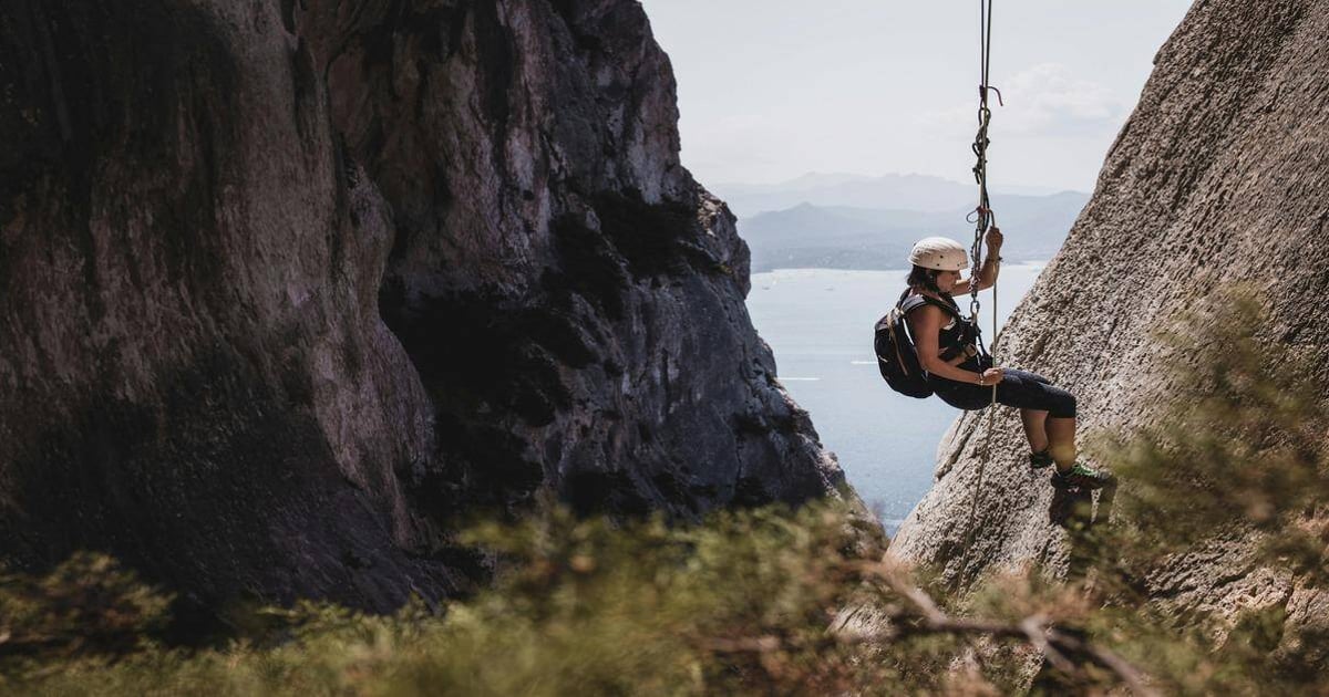 1. Female rock climber swinging on a mountain rescue swing with scenic landscape background.